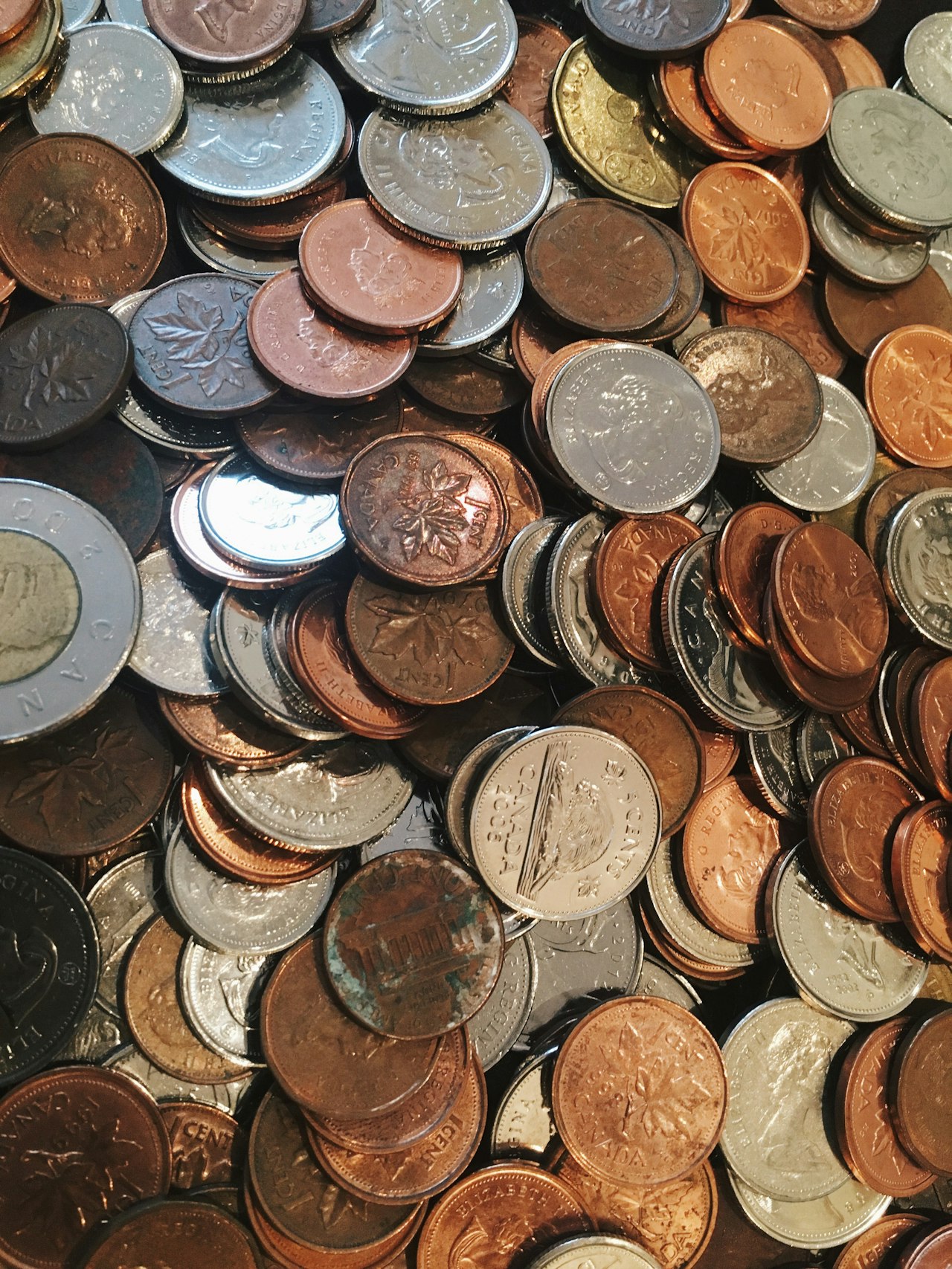 An overhead view of a large pile of mixed coins — pennies, dimes, quarters, and foreign currency — accumulated from many hunts